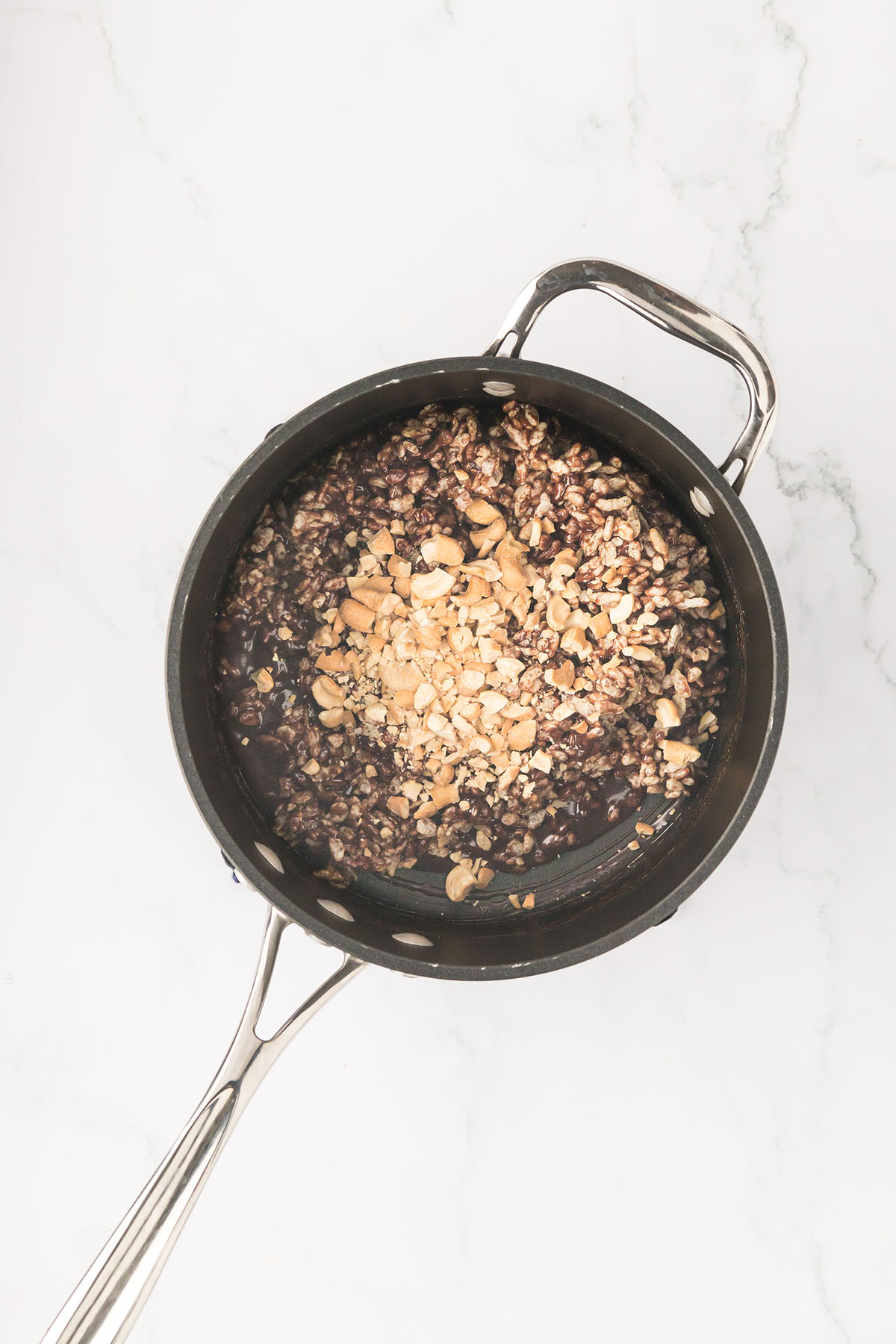 Cereal and cashews mixed into the chocolate caramel mixture in the saucepan.