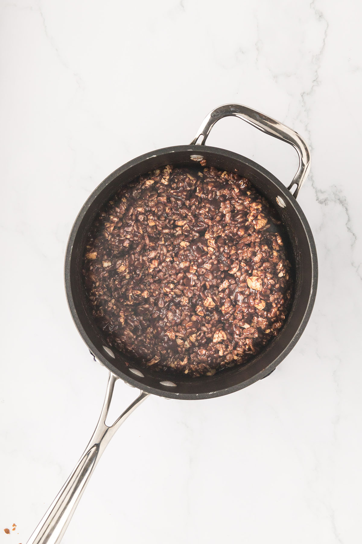 Chocolate chips, caramel dip, cereal and cashews are mixed together in the saucepan.