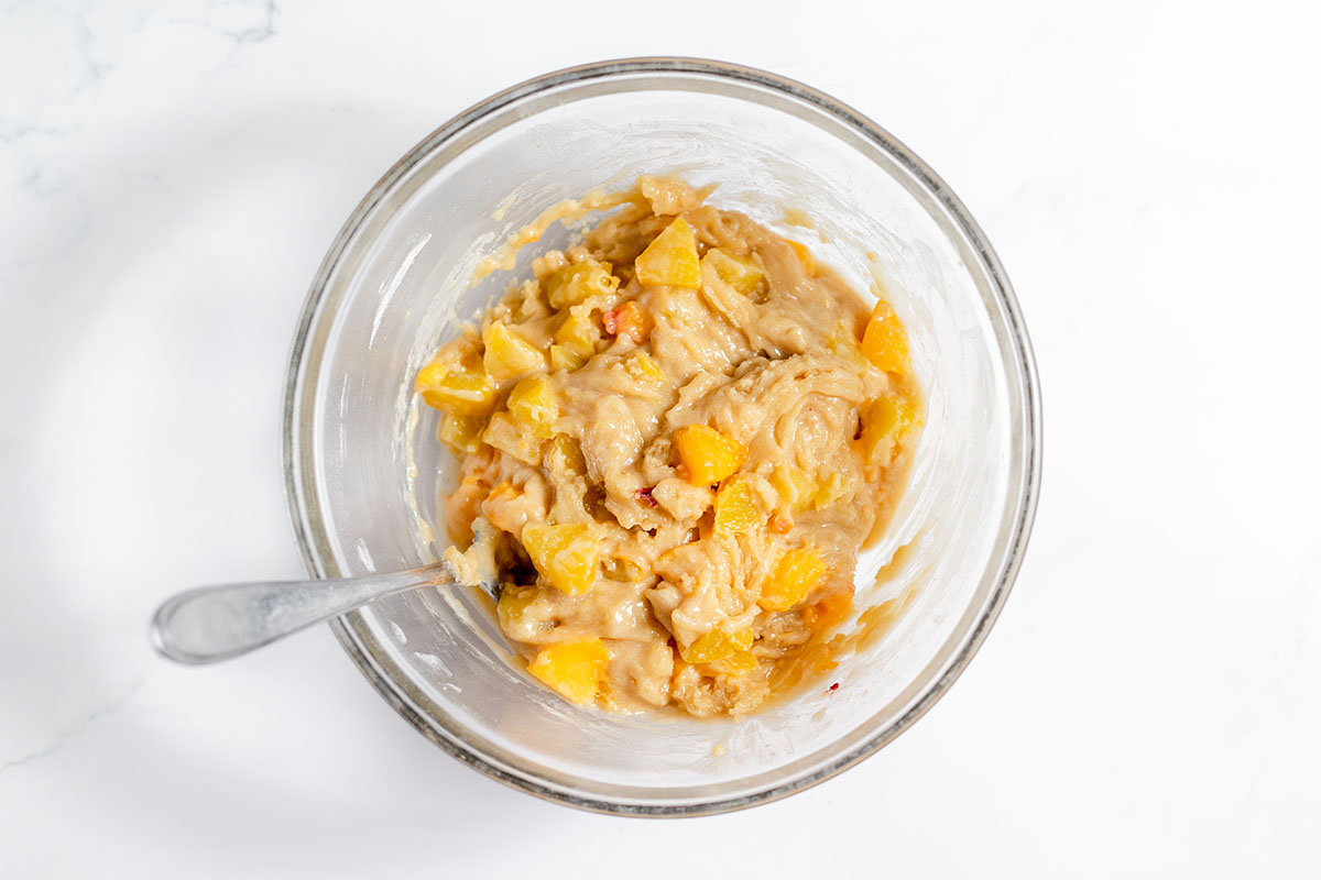 The diced peaches are folded into the batter in the mixing bowl.