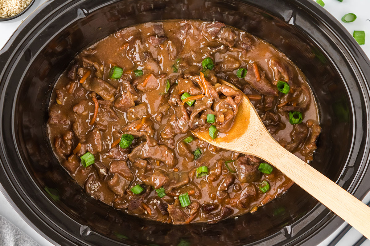 Mongolian beef in the slow cooker with a serving on a wooden spoon.