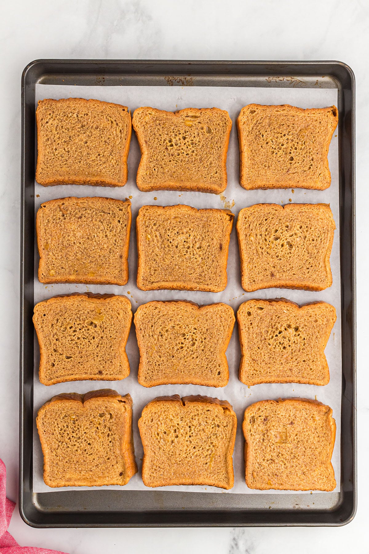 Gingerbread batter dipped bread on a parchment paper lined sheet pan.