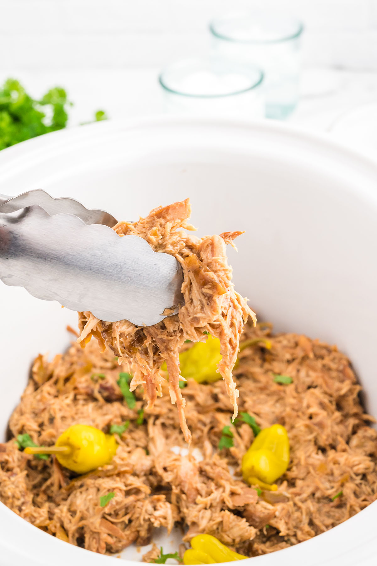 Mississippi chicken in the slow cooker with a serving on tongs.