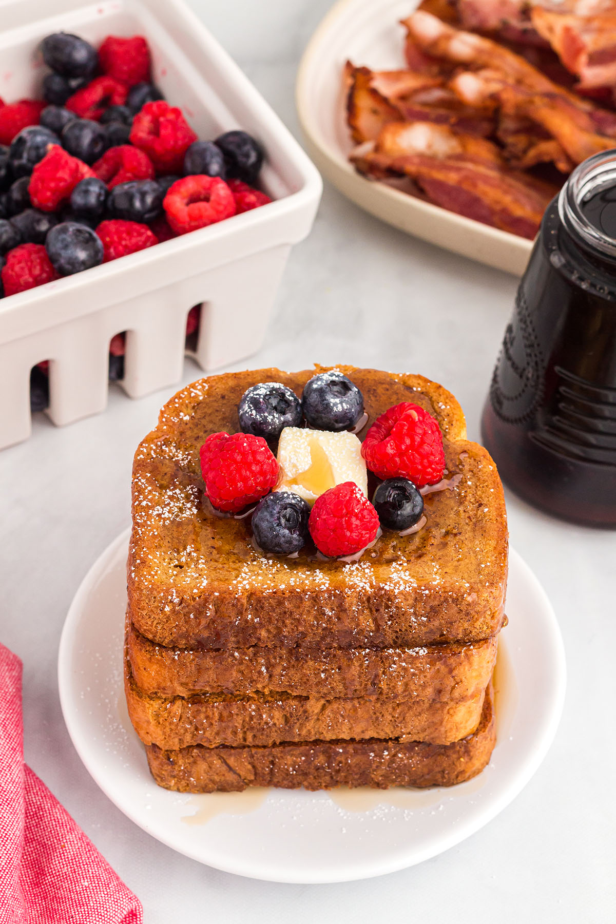 Gingerbread French toast slices stacked on a plate, topped with butter, berries, and syrup.