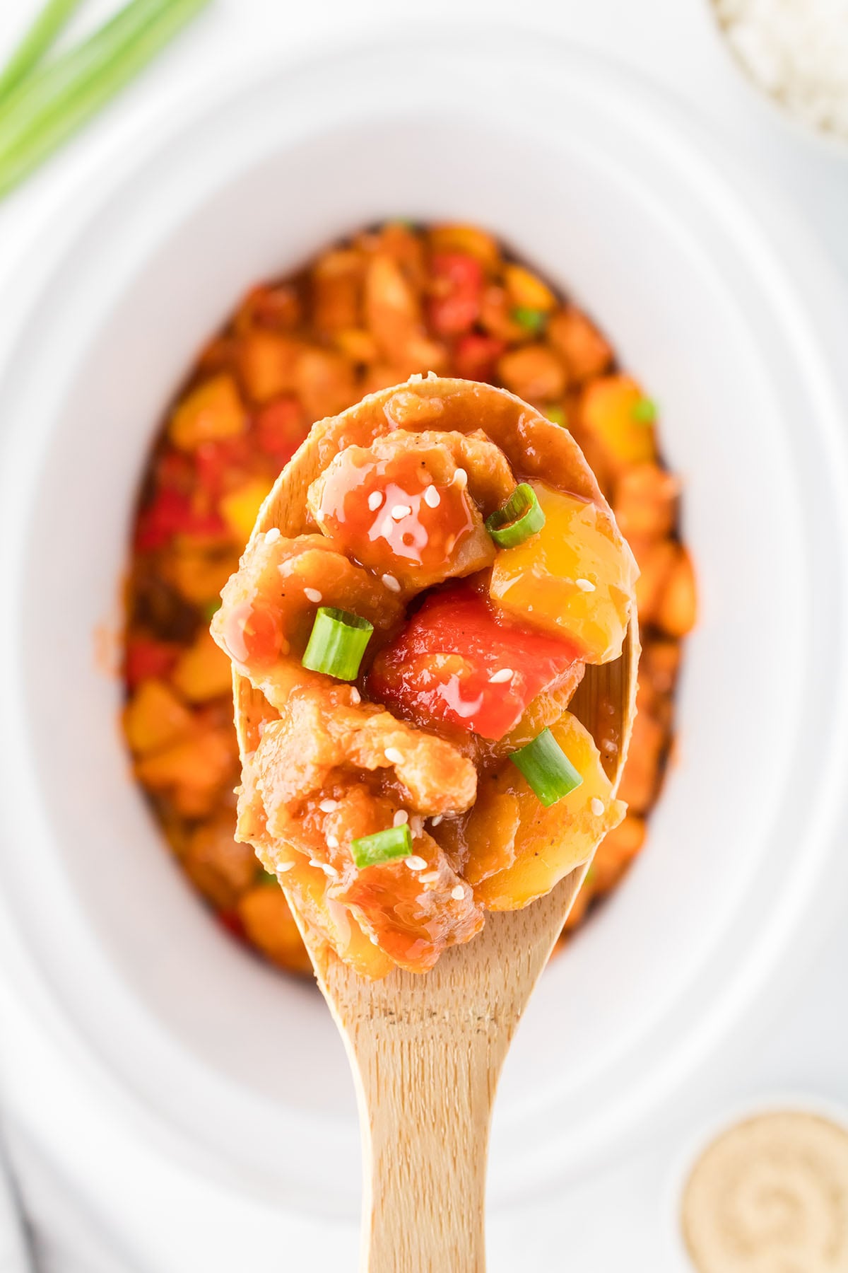Sweet and sour chicken being served with a wooden spoon.