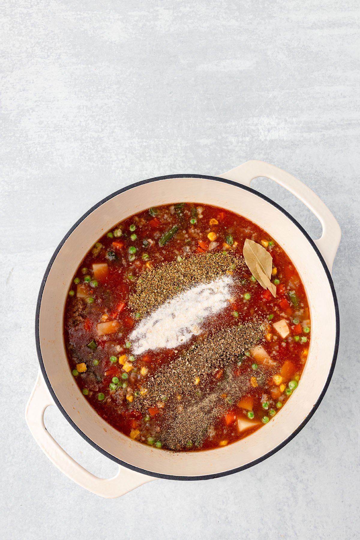 Basil, oregano, garlic, salt, black pepper, and bay leaf are added to the soup in the large pot.