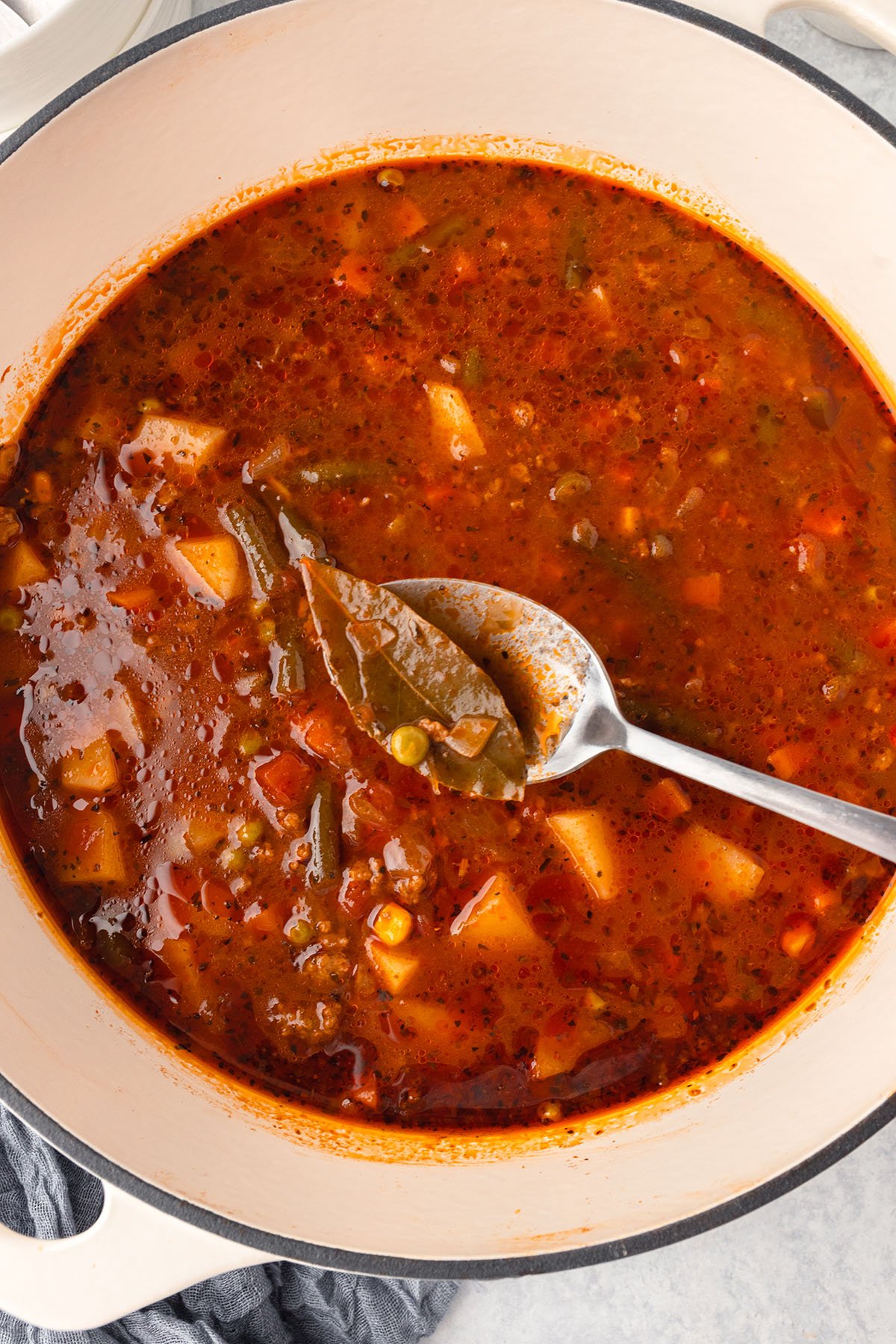 A bay leaf is removed with a spoon from the hamburger vegetable soup in the large pot.