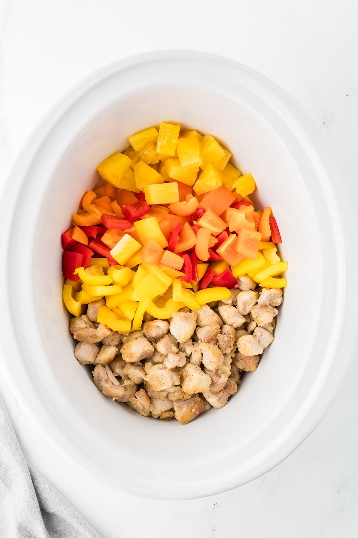 The browned chicken, bell peppers, and pineapple chunks are added to the slow cooker.
