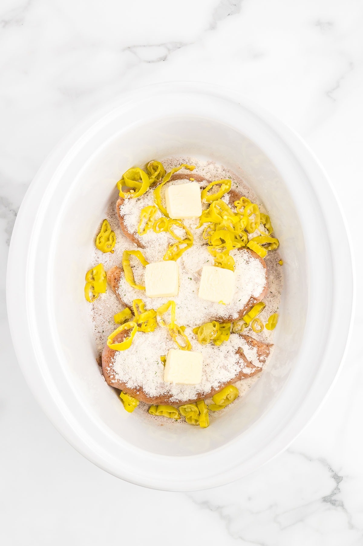 Chicken breast, au jus gravy mix, ranch dressing mix, butter, and sliced pepperoncini peppers in a slow cooker.