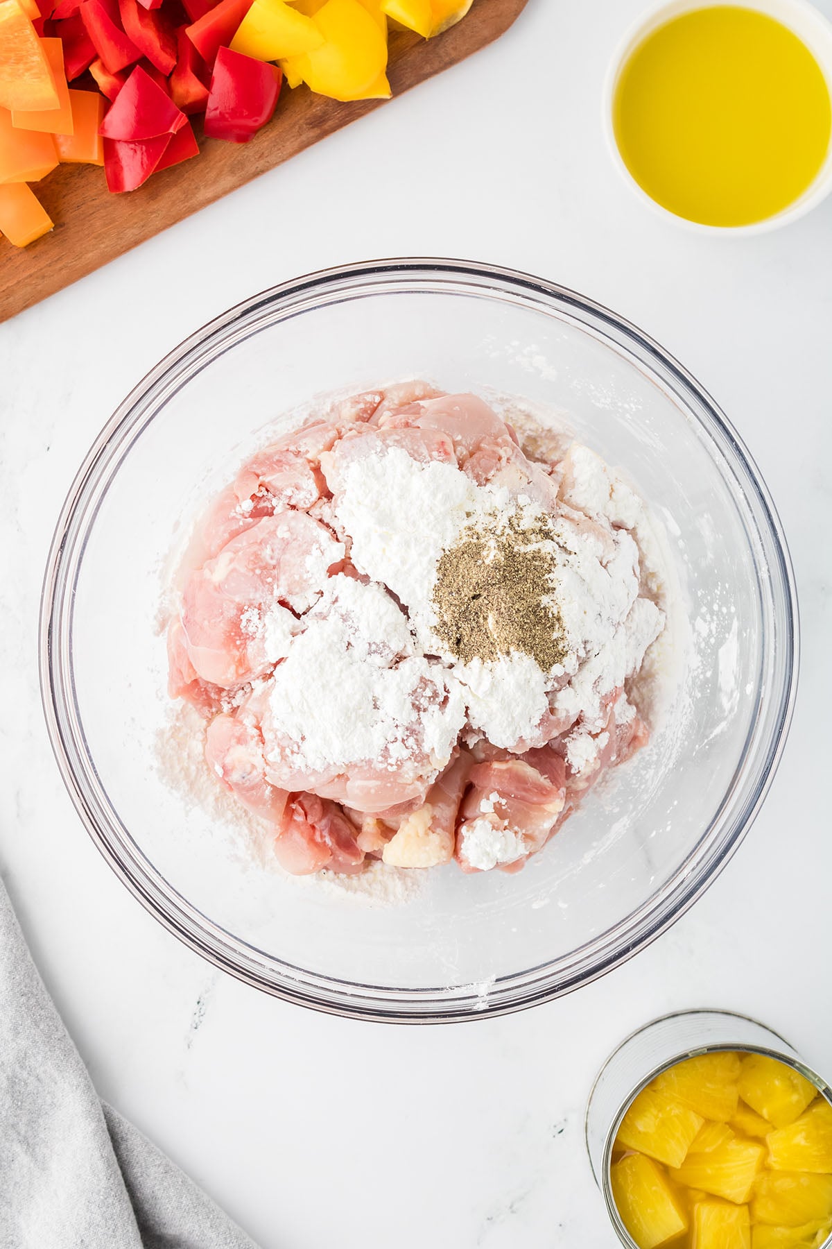 Chicken tossed with cornstarch and pepper in a glass mixing bowl.