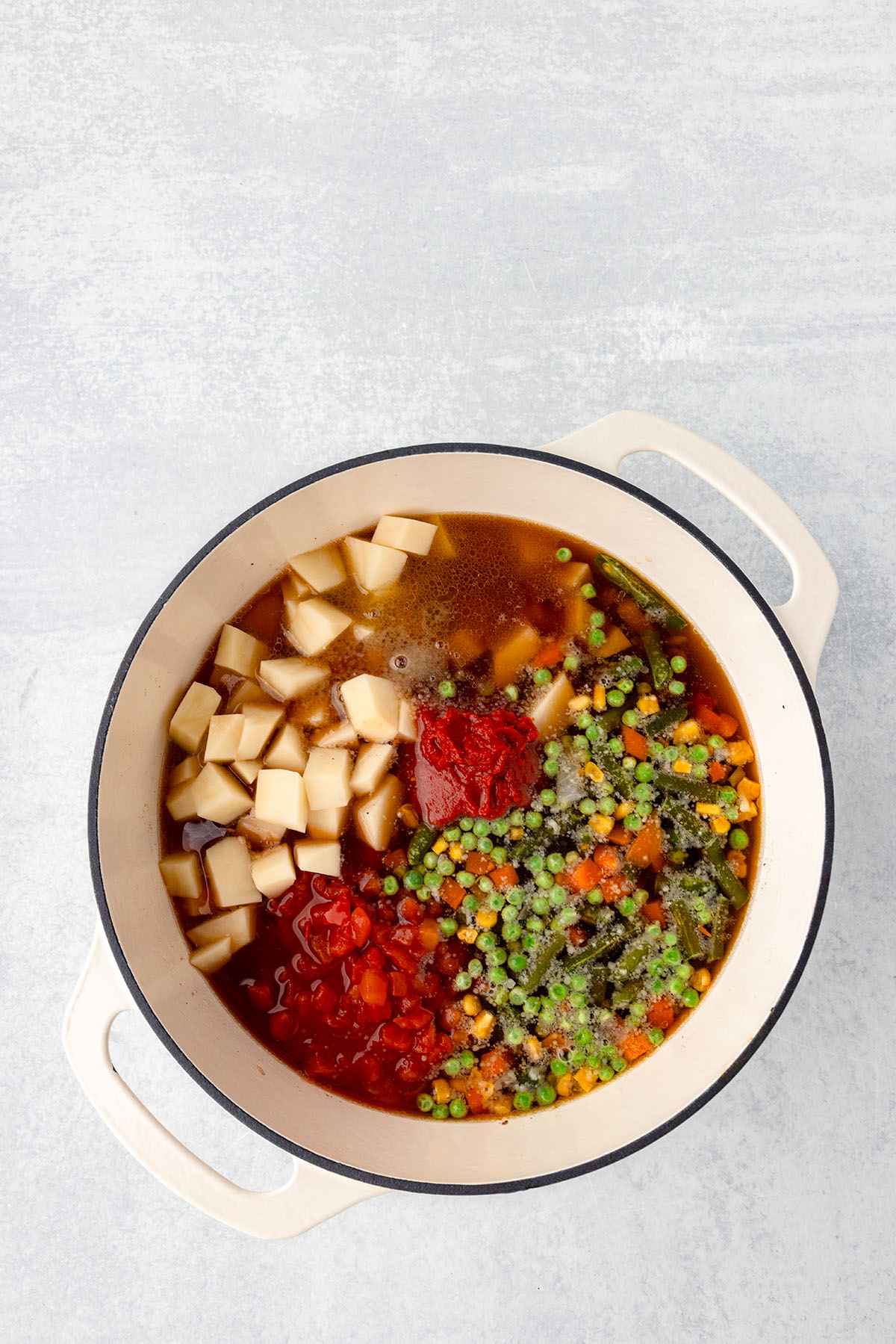 Mixed vegetables, diced potatoes, beef broth, diced tomatoes, tomato paste, and seasonings are added to ground beef in the large pot.