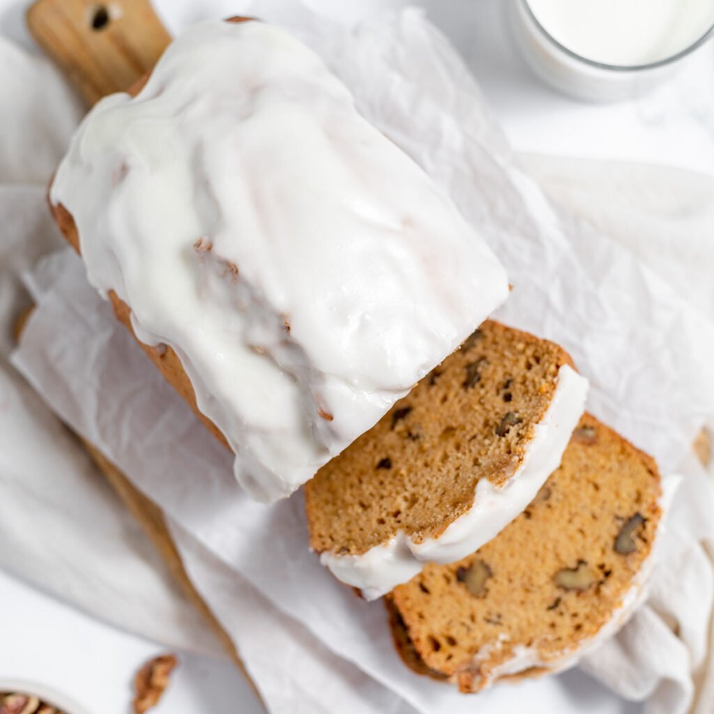Sweet potato bread topped with icing and two slices cut on a wooden serving board.