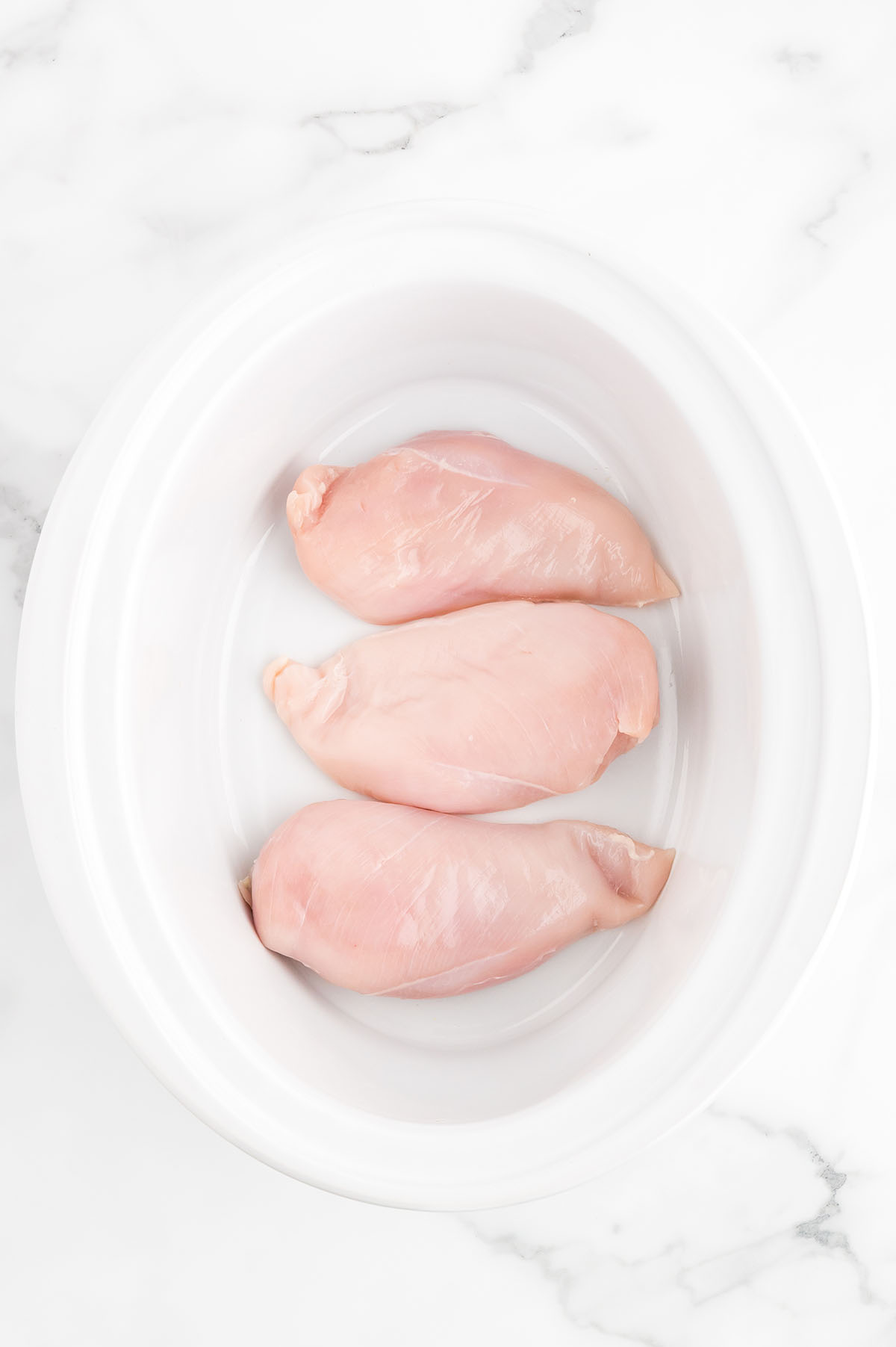 Raw chicken breast at the bottom of the slow cooker.