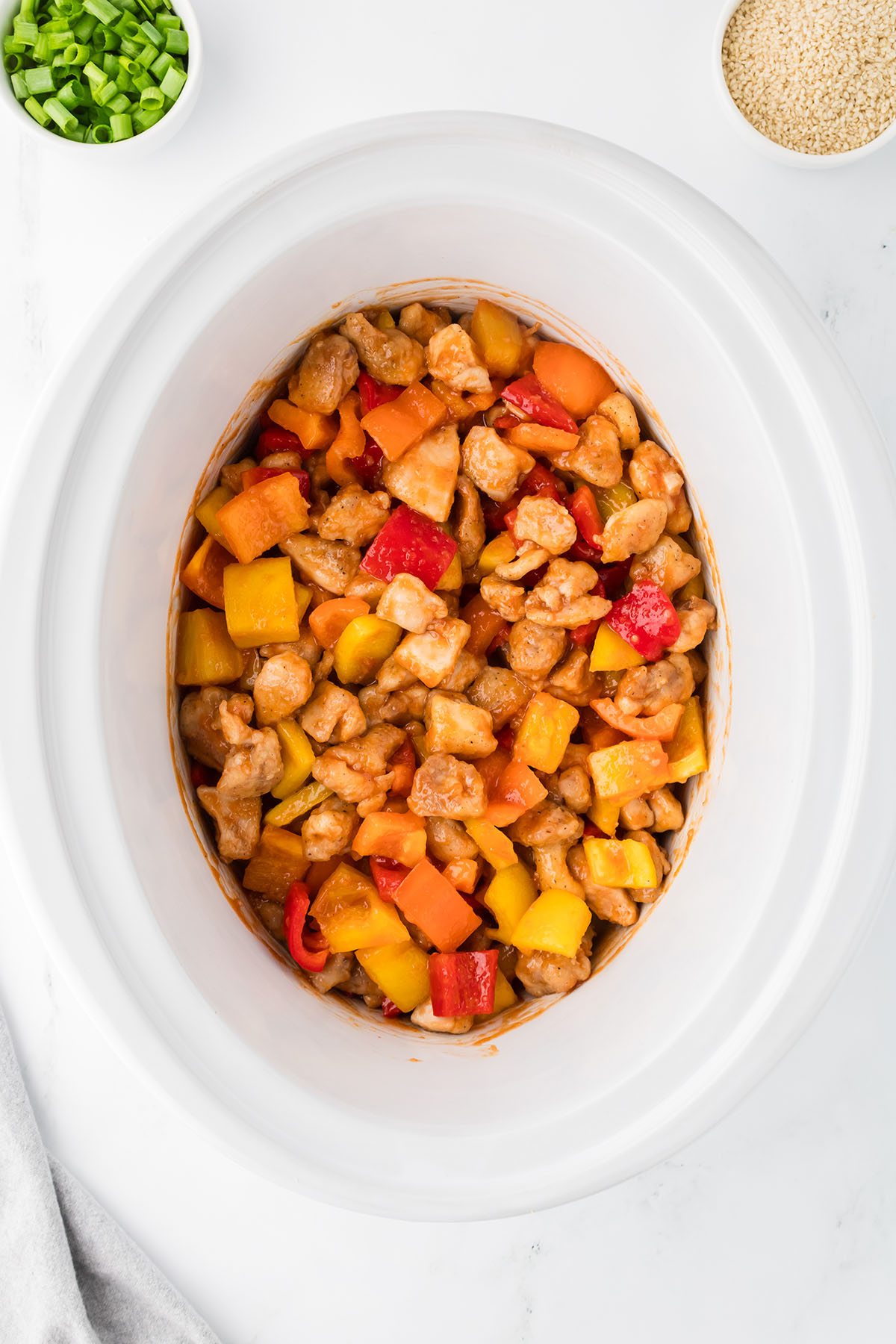 The sweet and sour sauce is tossed with the chicken, bell peppers, and pineapples in the slow cooker.