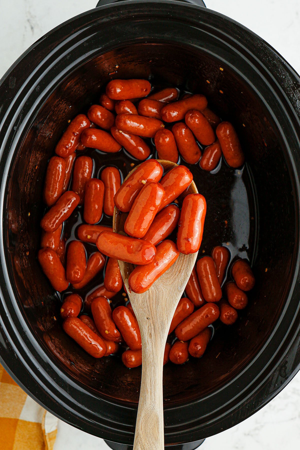 Honey BBQ Little Smokies in the slow cooker and a serving on a wooden spoon.