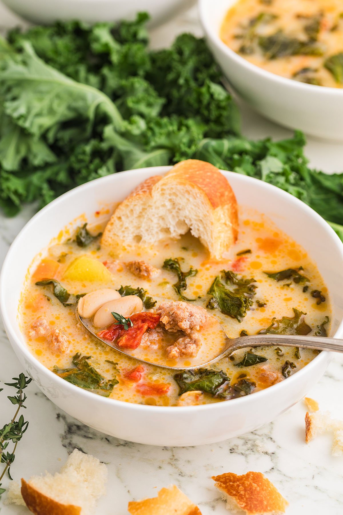 A serving of Kale and Sausage Soup in a white bowl with crusty bread.