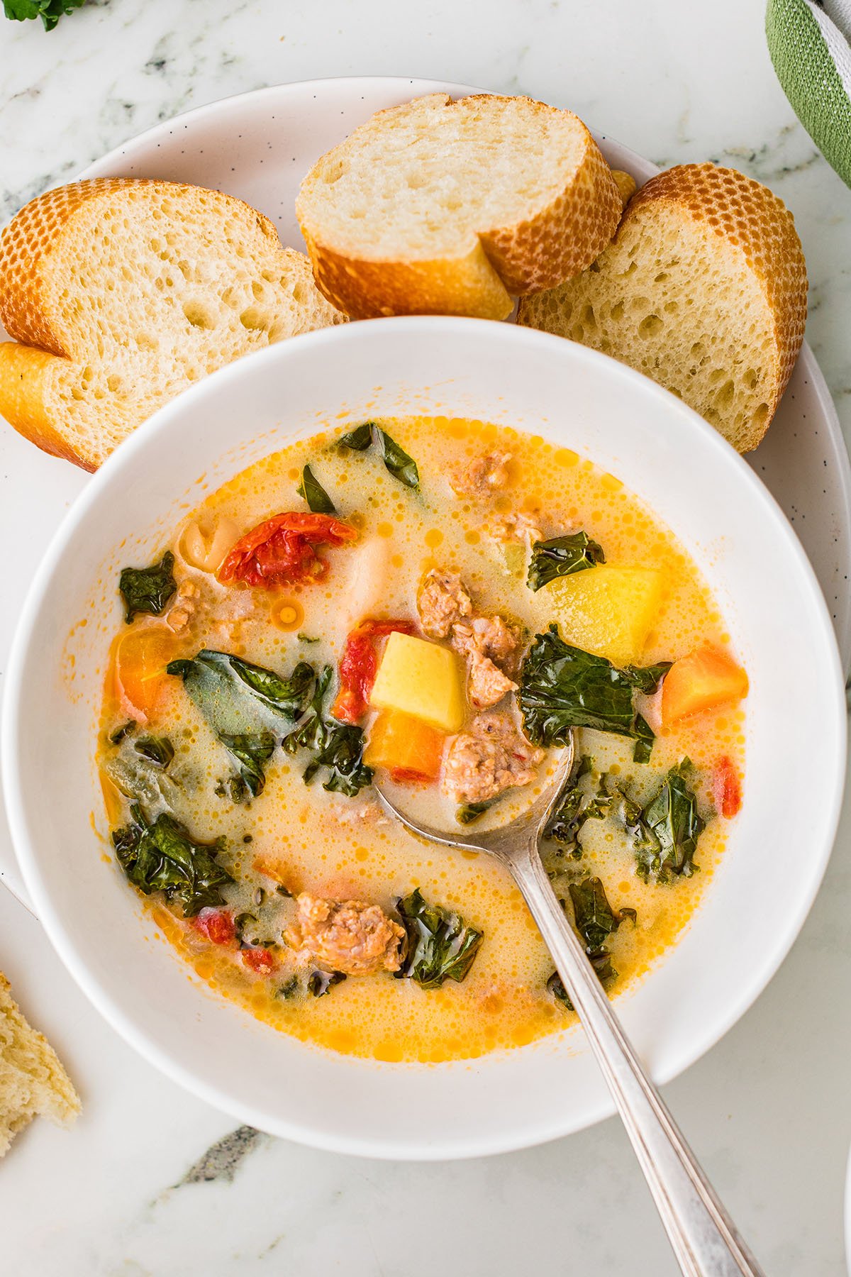 Sausage and Kale Soup served in a white bowl with a bite on a spoon.
