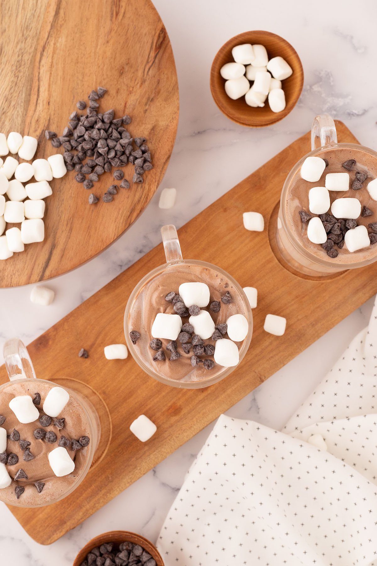 Whipped Hot Chocolate in three glasses on a wooden serving board.