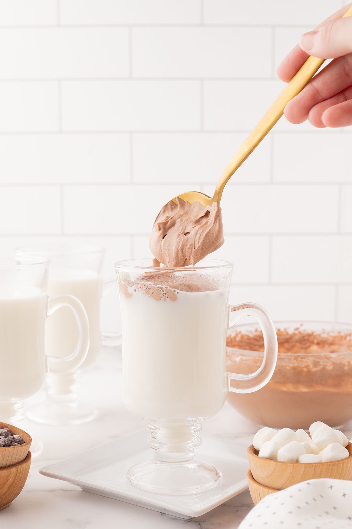 Whipped Hot Chocolate is added to milk in a drinking glass.