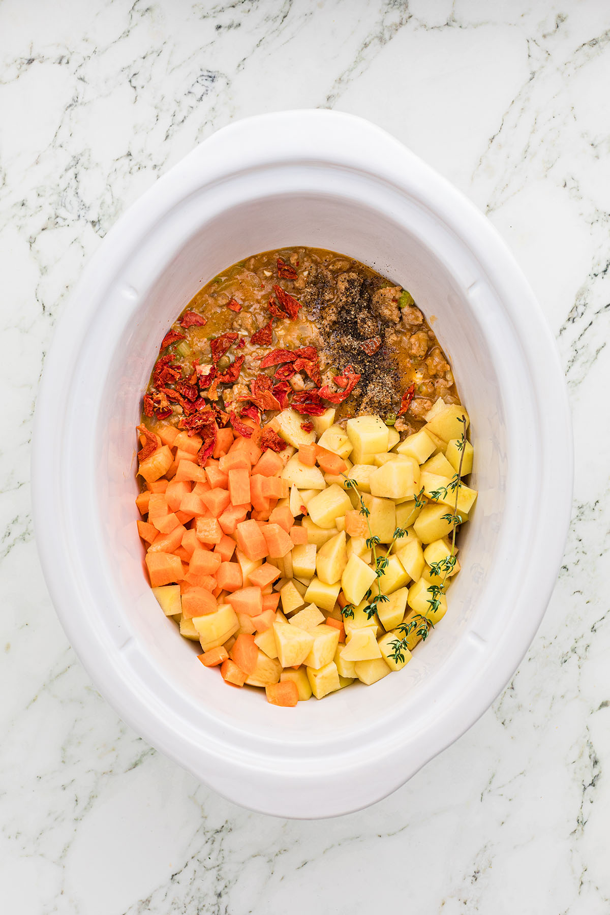 Browned sausage, thyme, black pepper, sun-dried tomatoes, carrots, and potatoes in the slow cooker.