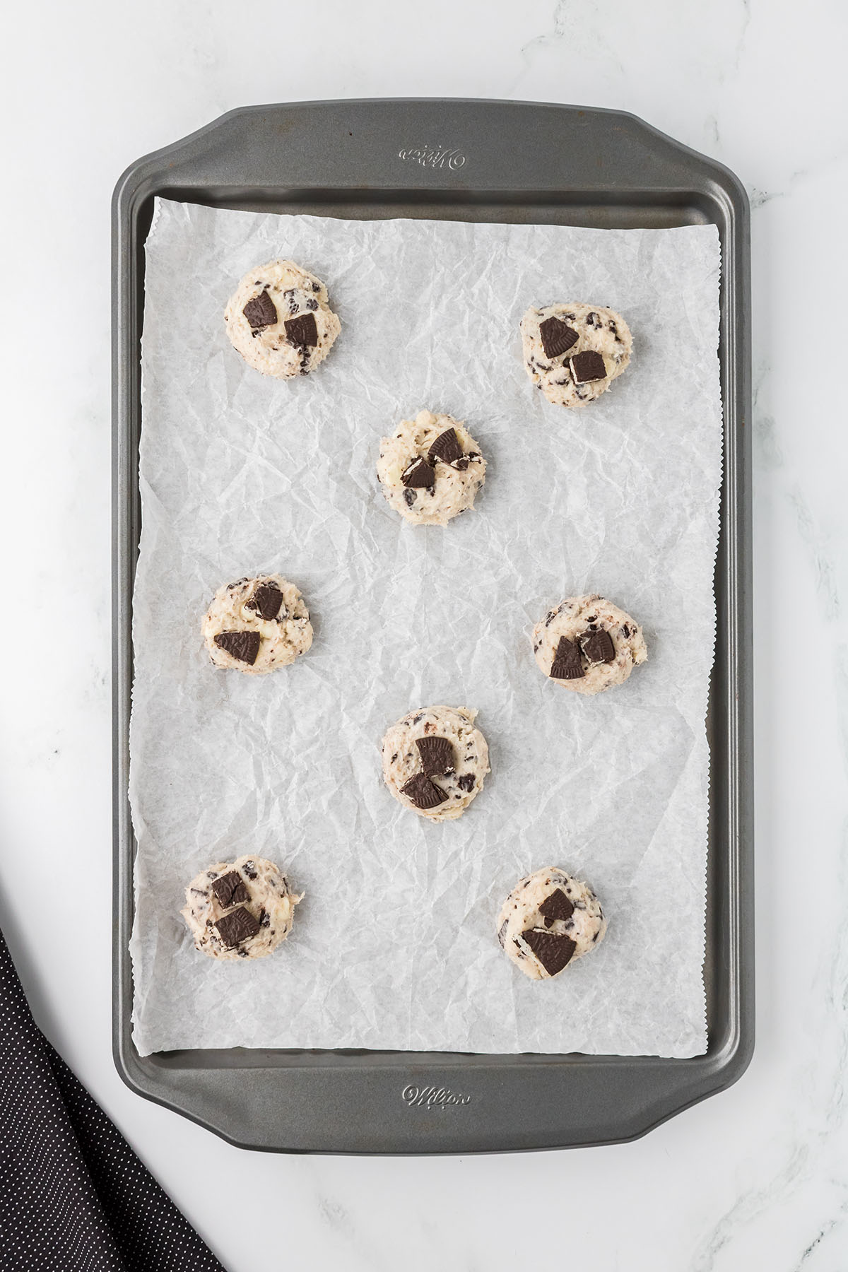 Crushed Oreos are placed on top of the cookie dough balls on the baking sheet.