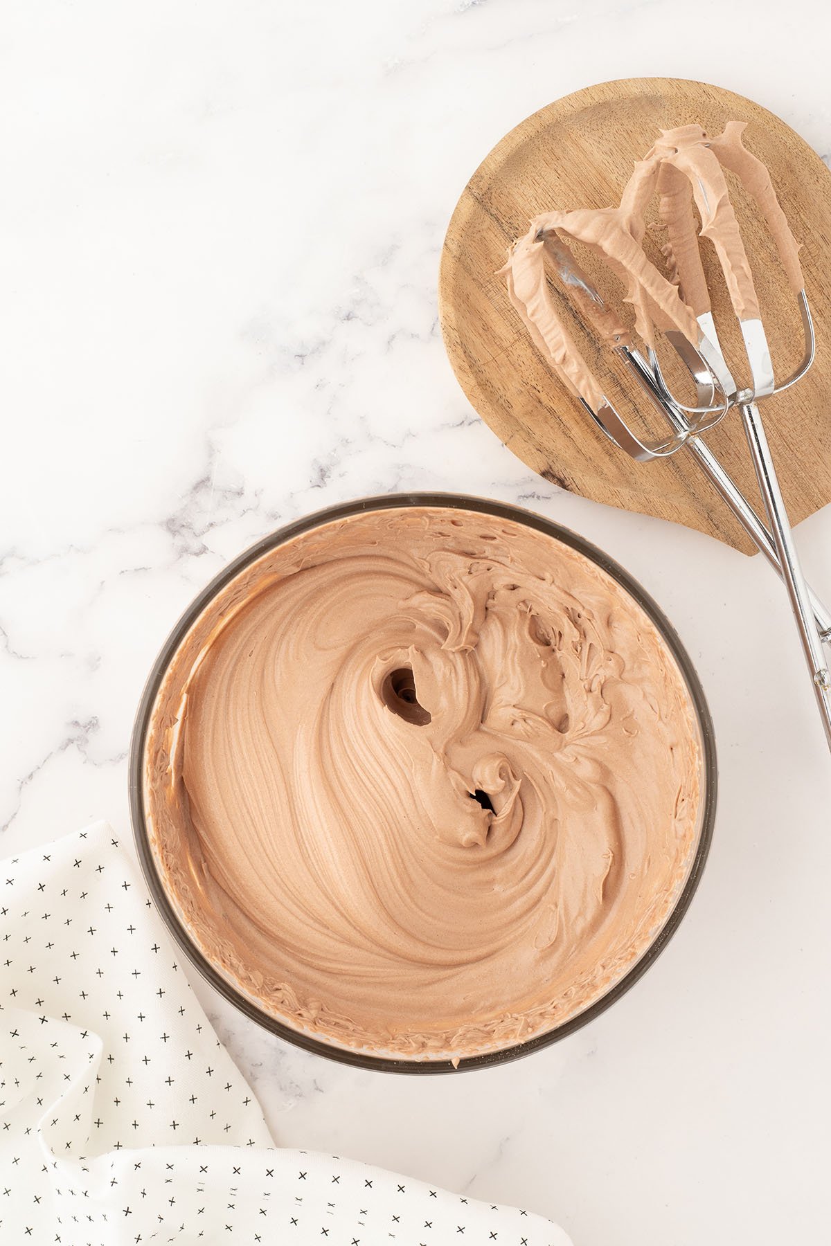 Hot chocolate mix and whipping cream are beaten to stiff peaks in a glass mixing bowl.