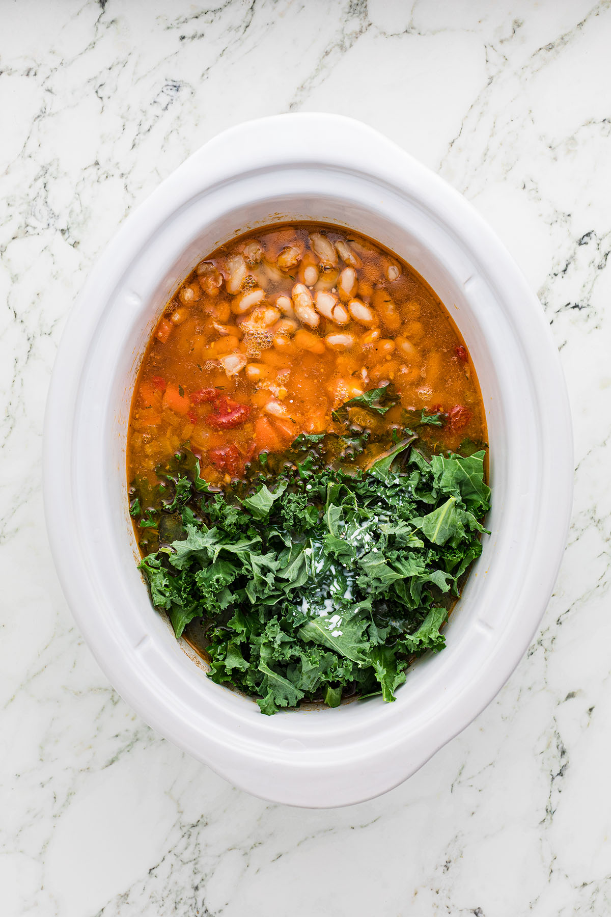 Kale added to the sausage, chicken broth, and vegetables in the slow cooker.