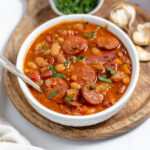 A bowl of 15 bean sausage soup on a round wooden serving board.