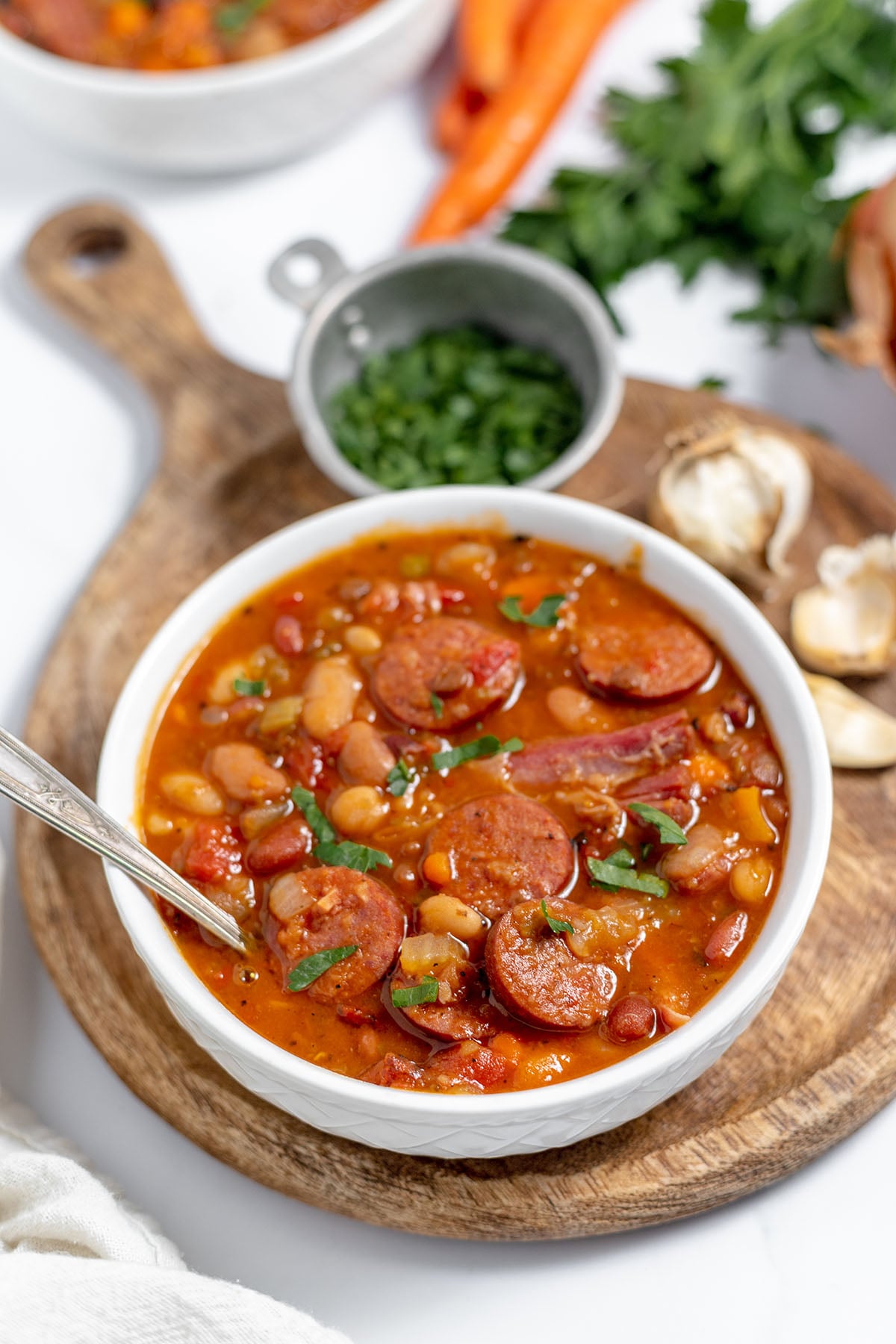 A bowl of 15 bean sausage soup on a round wooden serving board.