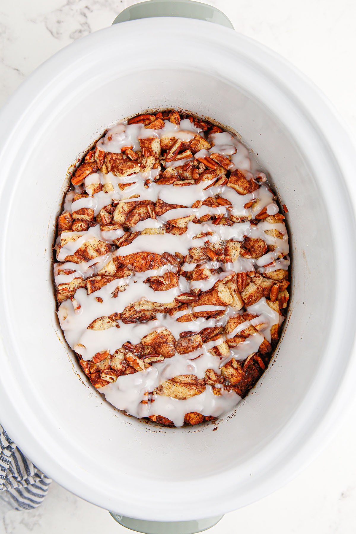 Cinnamon Roll Casserole topped with icing in the slow cooker.