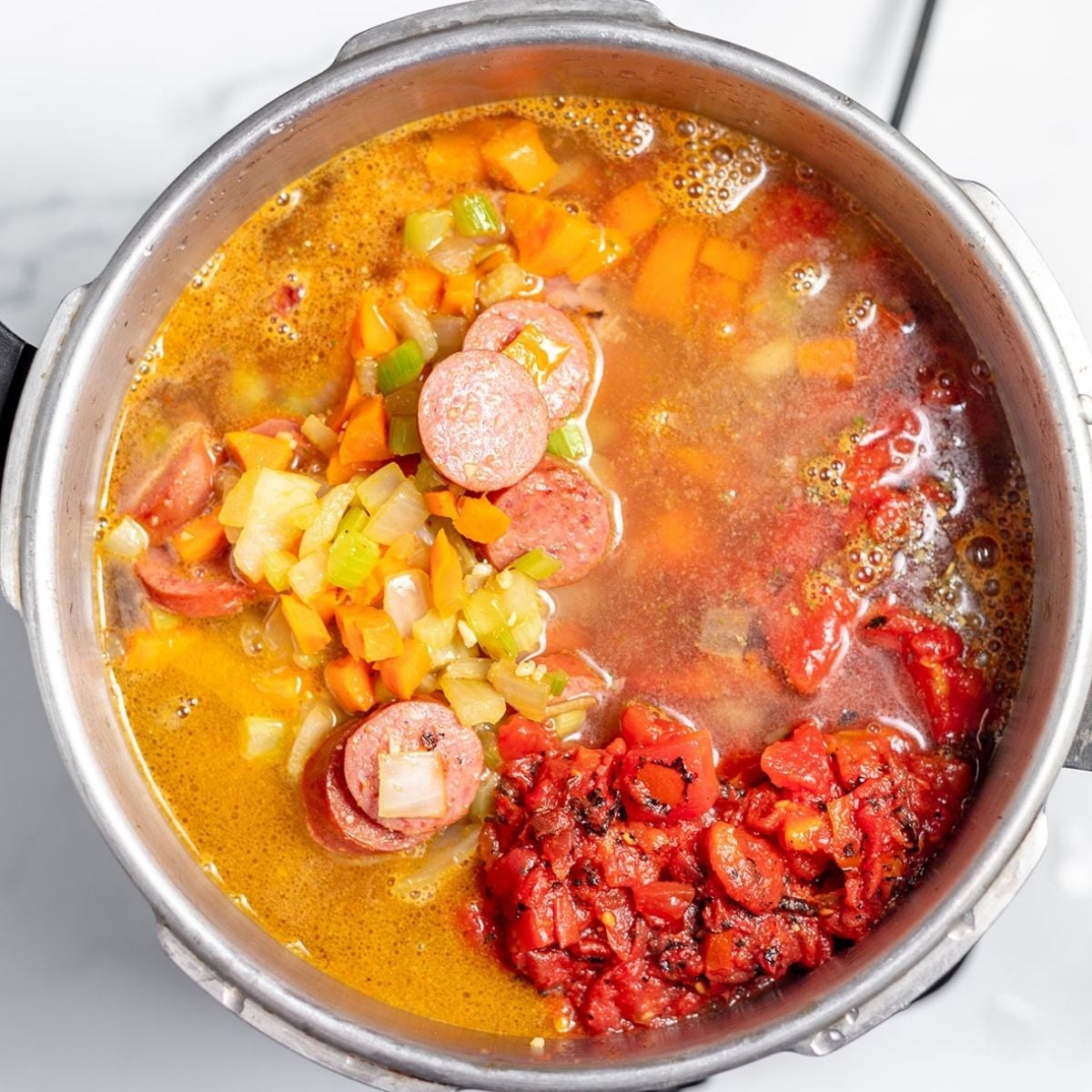 Beans, sausage, vegetables, diced tomatoes, chicken broth, and seasoning in a large pot.