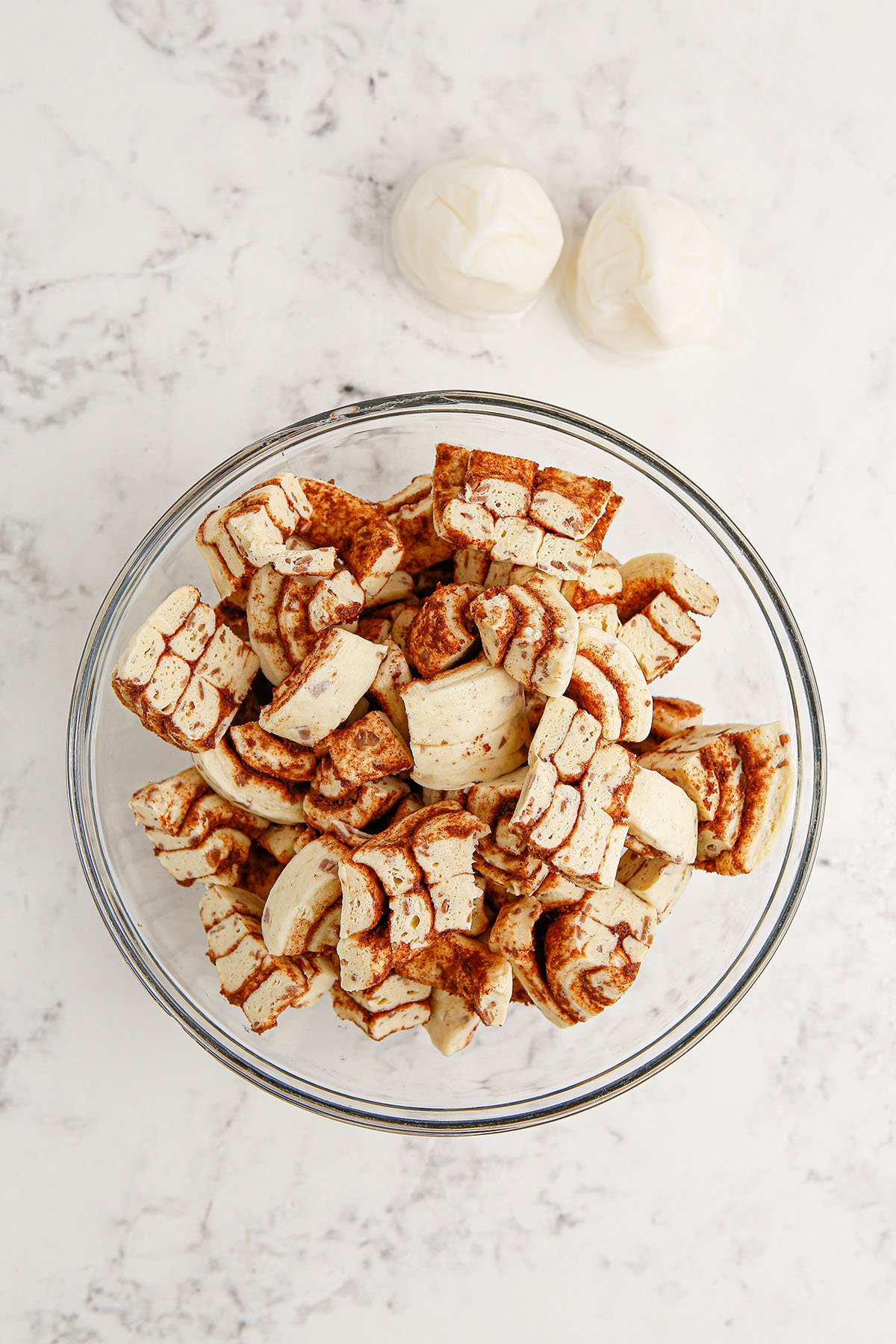 Cinnamon rolls are cut into quarters and placed in a mixing bowl.