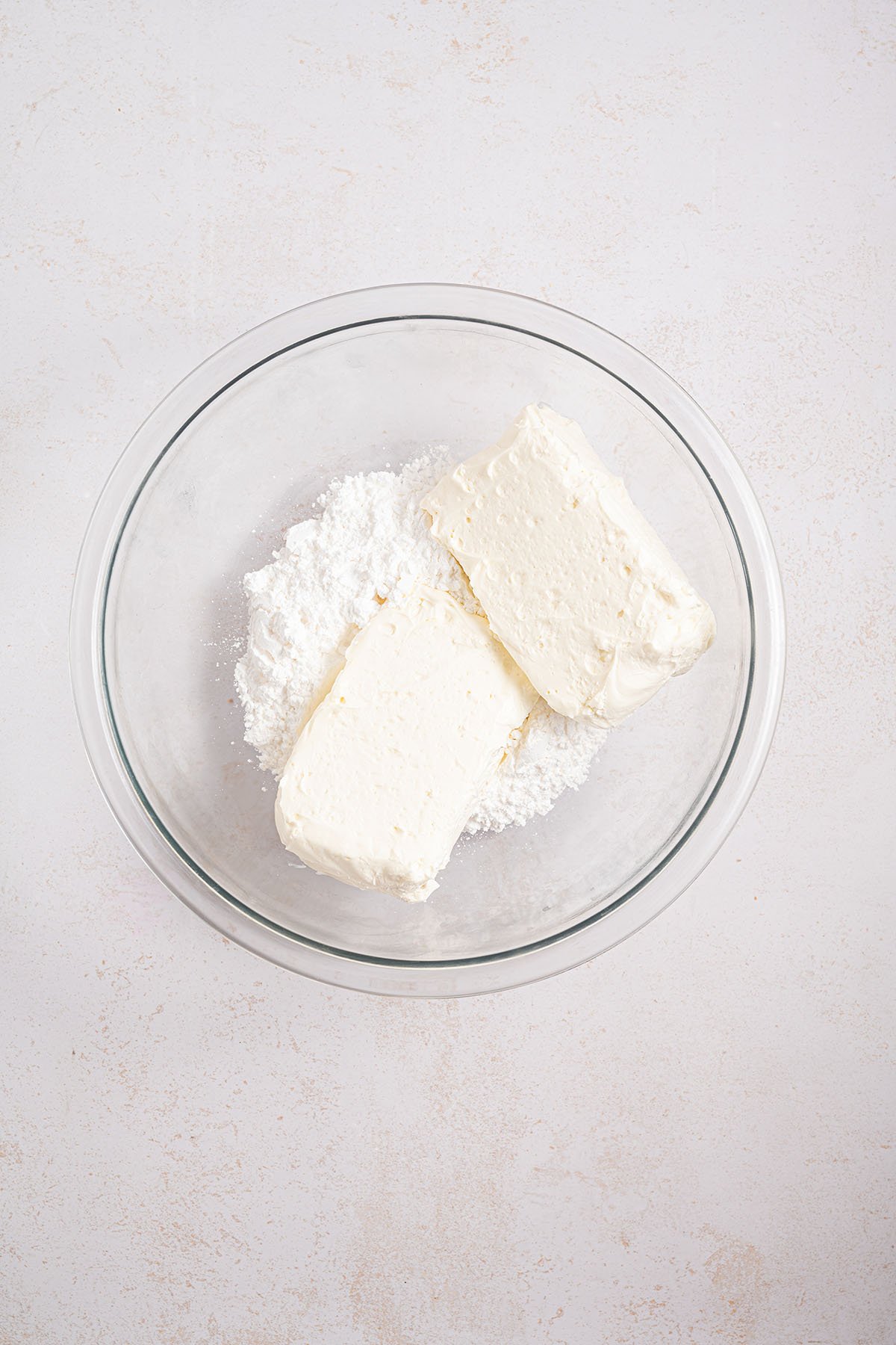 Cream cheese and powdered sugar in a glass mixing bowl.