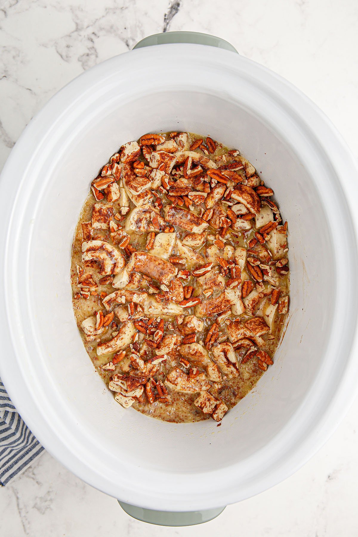 Pecans sprinkled over the cinnamon roll mixture in the slow cooker.