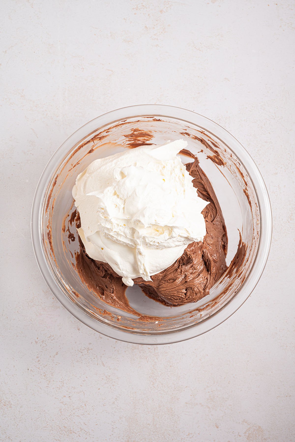 Whipped topping added to the chocolate cream cheese mixture in the glass mixing bowl.