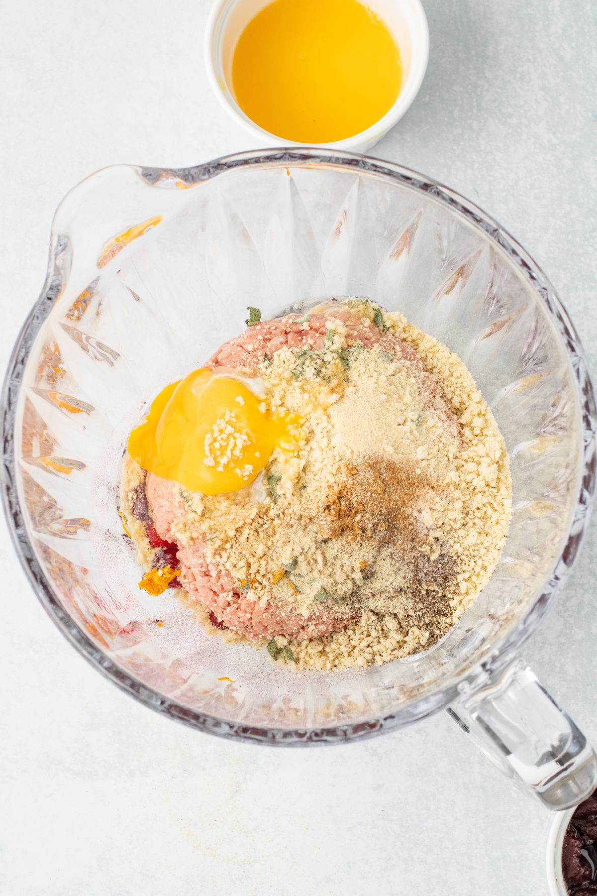 Cranberries, ground turkey, seasonings, eggs, and breadcrumbs in a glass mixing bowl.
