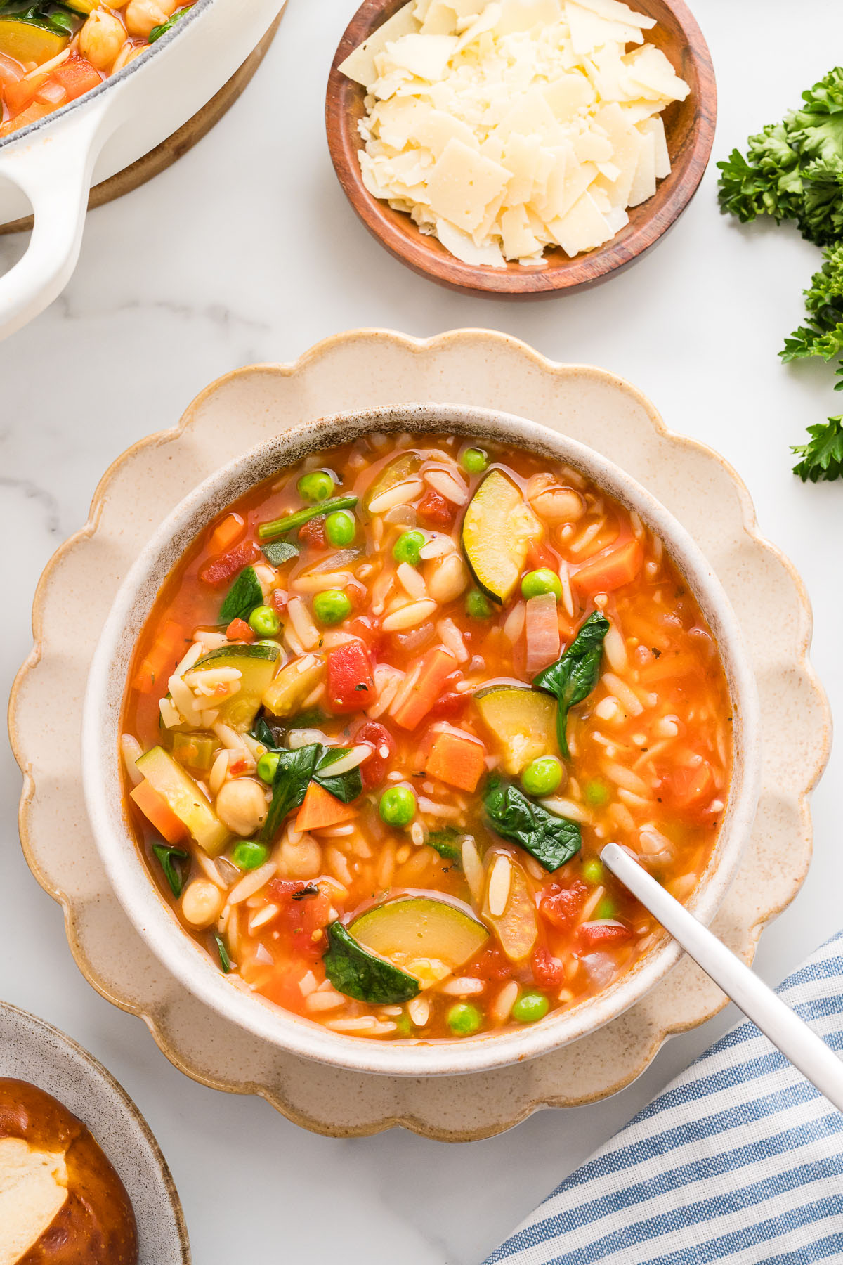 Vegetable orzo soup served in a white bowl with a spoon.