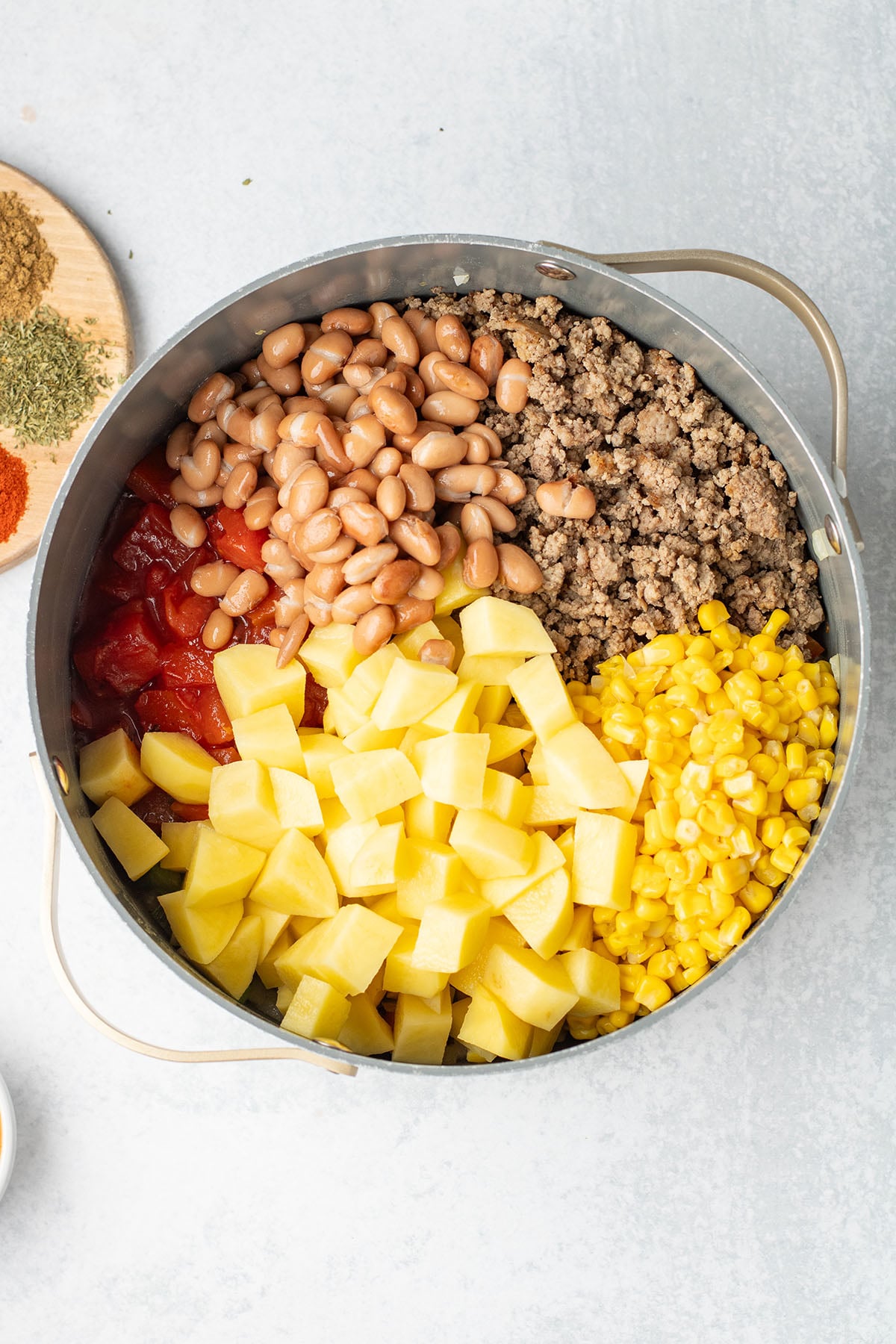 Ground beef, corn, pinto beans, fire-roasted tomatoes, diced potatoes, and tomato sauce in a large pot.