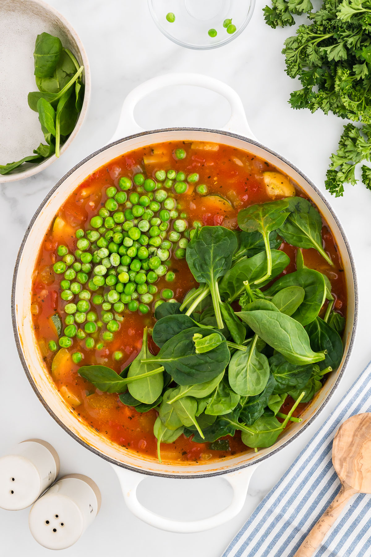 Fresh spinach and frozen peas are added to the soup in the large pot.
