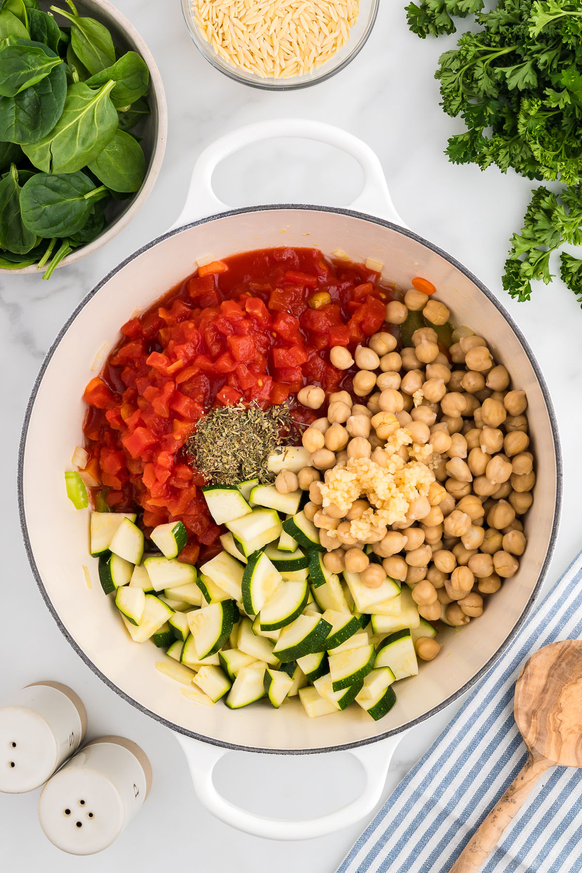 Zucchini, diced tomatoes, garlic, Italian seasoning, and garbanzo beans are added to sauteed vegetables in a large pot.