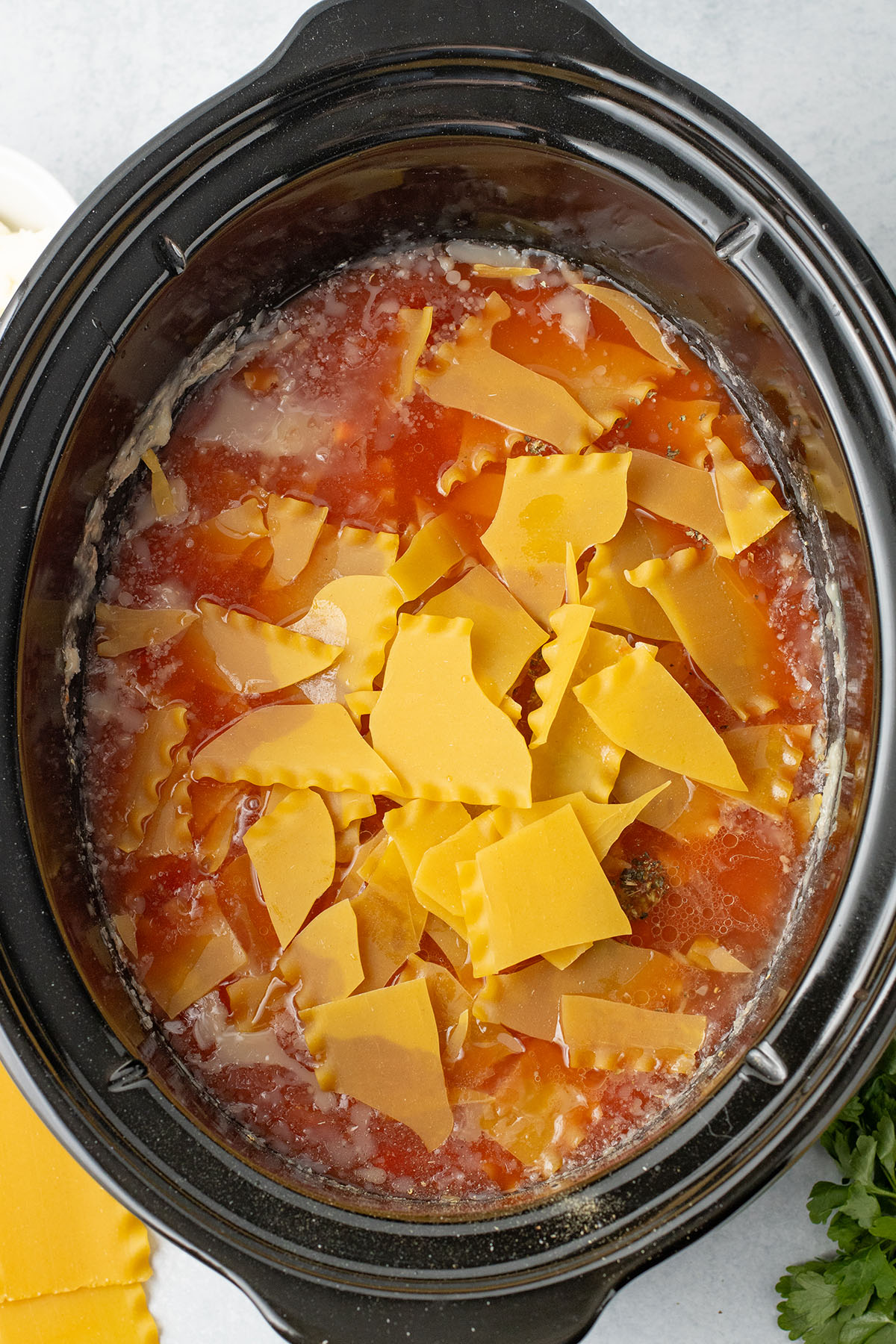 Broken lasagna noodles are added to the soup in the slow cooker.