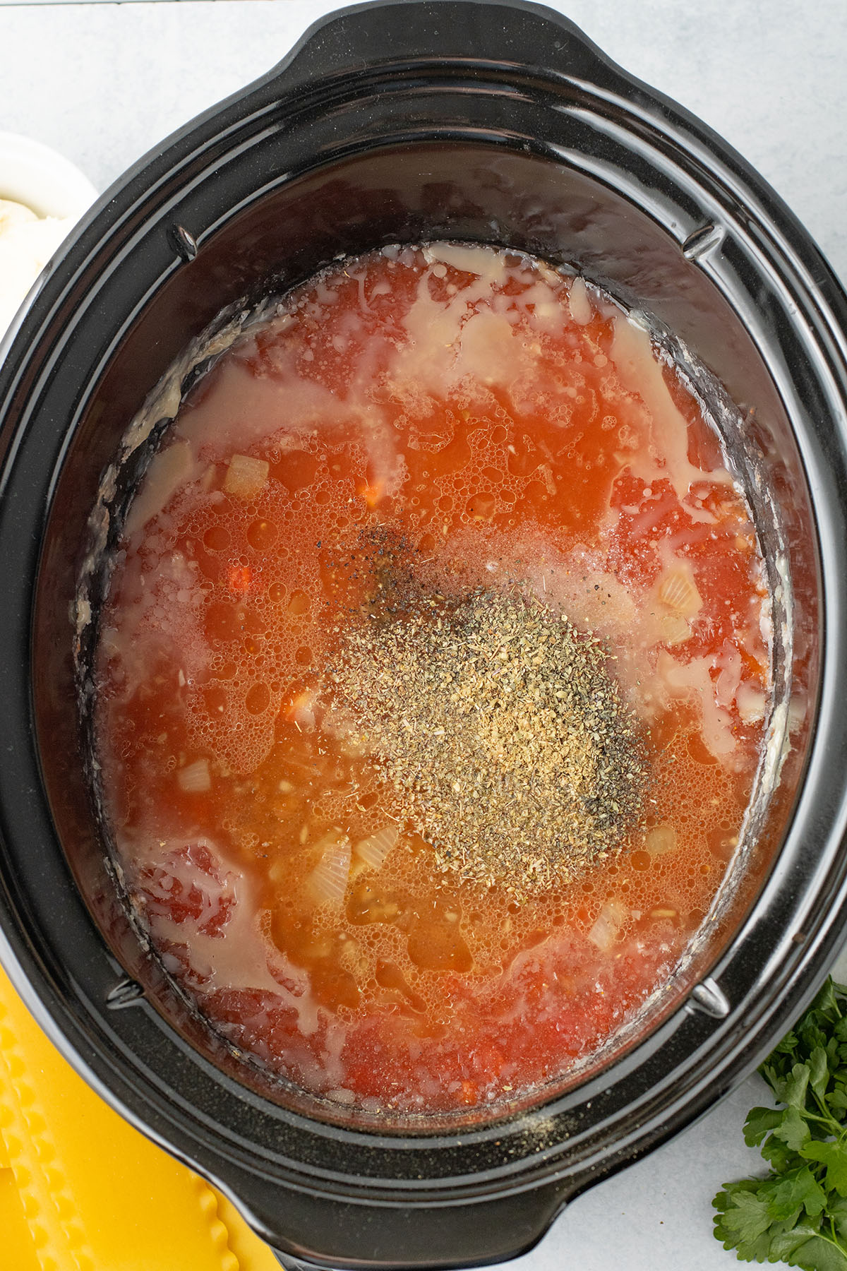 Cooked ground beef, diced tomatoes, crushed tomatoes, vegetable broth, oregano, basil, salt, and pepper are added to the slow cooker.