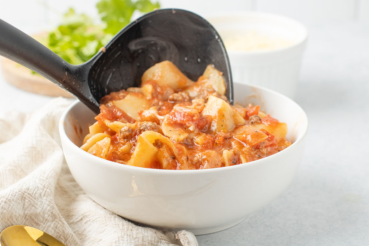 Ladling lasagna soup into a white bowl.