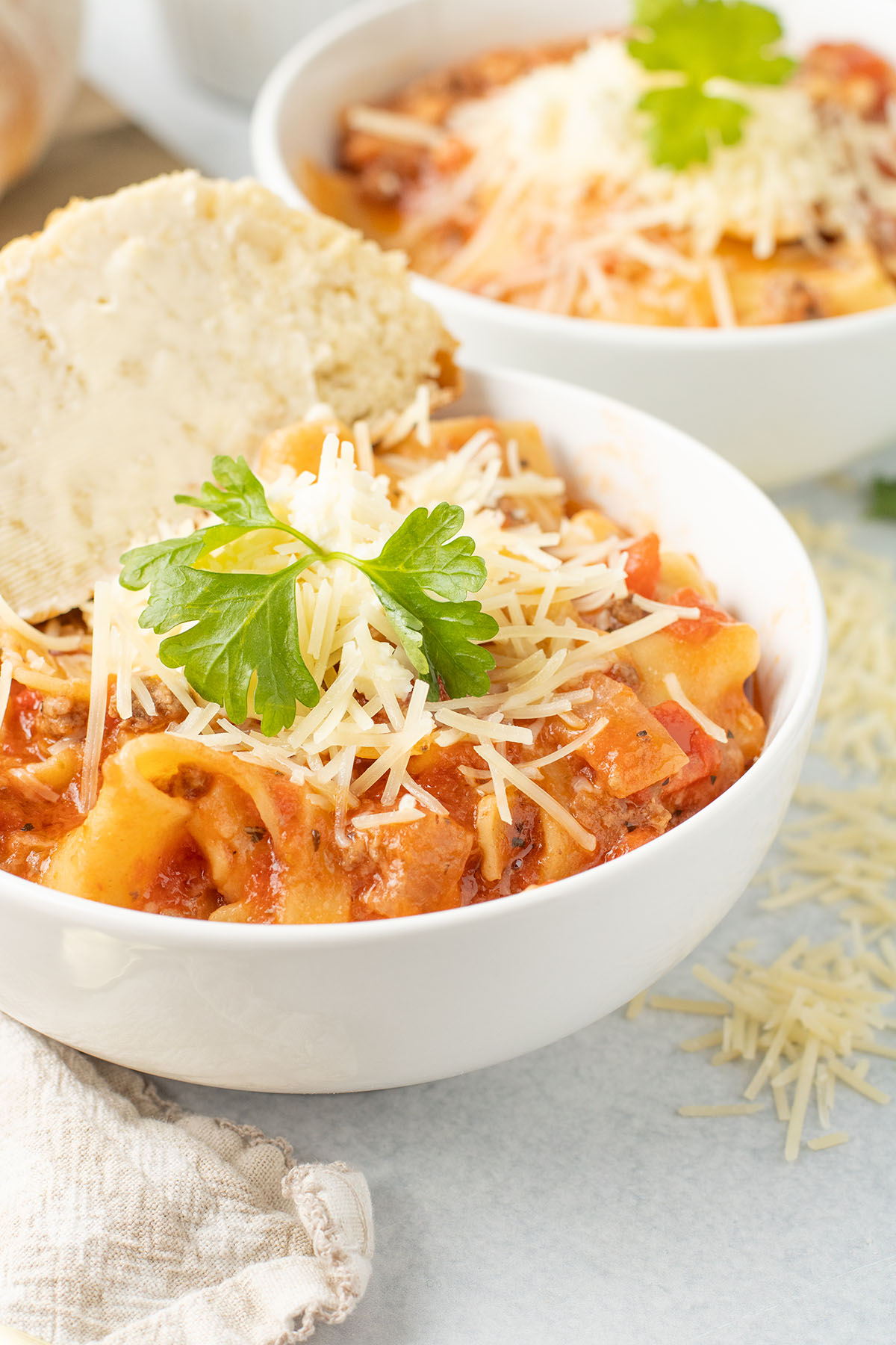 Lasagna soup topped with Parmesan cheese and Parsley is served in a white bowl.